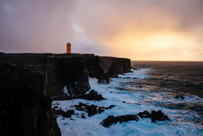 Rocky shore by sea against sky during sunset