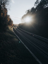 Railroad tracks by road against sky during sunset