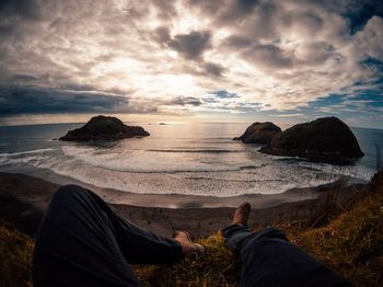 Low section of people on rocks at beach against sky