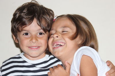 Close-up portrait of boy with cheerful sister against white background