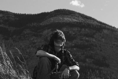 Woman looking at while sitting on land against sky