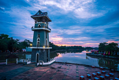 Traditional building by lake against sky at sunset