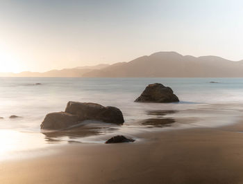 Rocks on beach against sky during sunset