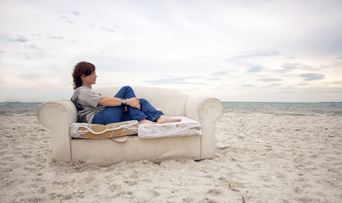 Woman sitting on beach against sky