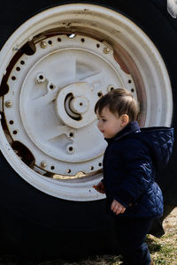 High angle view of boy standing next to a giant tractor wheel