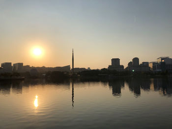 Silhouette buildings by lake against sky during sunset