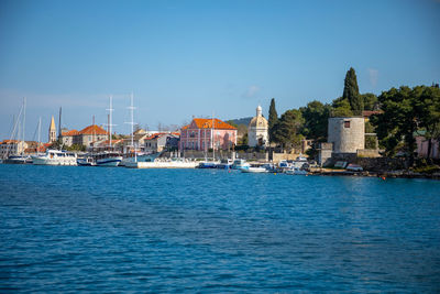 Sailboats in sea by buildings against clear blue sky