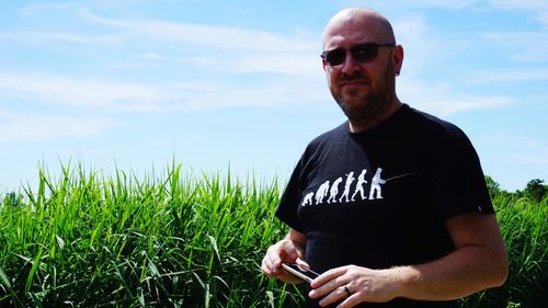 Portrait of bald man wearing eyeglasses standing on field against sky during sunny day