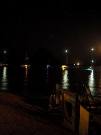 Illuminated city by river against sky at night