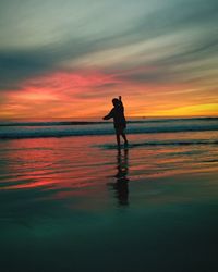 Silhouette woman standing on shore against sky during sunset