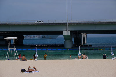 People on beach by bridge against sky
