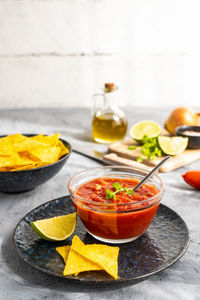 Tomato dip with nachos tortilla in bowl and main ingredients aside