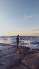 Side view of man standing at beach against sky during sunset