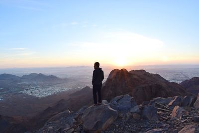 Man standing on rock against sky during sunset