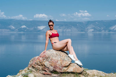 Young girl in a red swimsuit sits on a stone by the sea