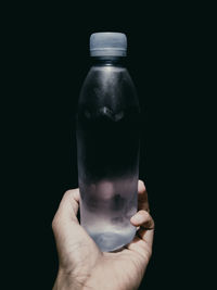 Close-up of hand holding glass bottle against black background