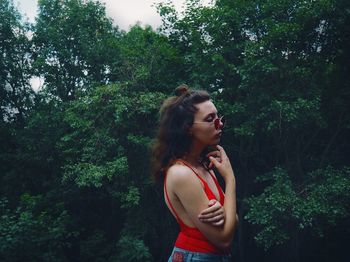 Young woman looking away while standing by tree in forest