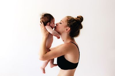 Woman kissing while holding daughter against white background