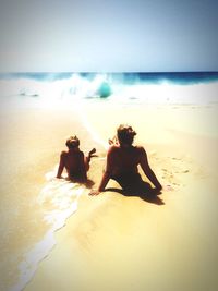 Rear view of woman relaxing with daughter at sea shore