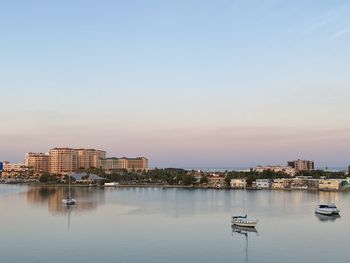 Sailboats in sea by buildings against clear sky