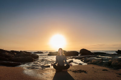 Young woman meditating on shore at beach during sunset