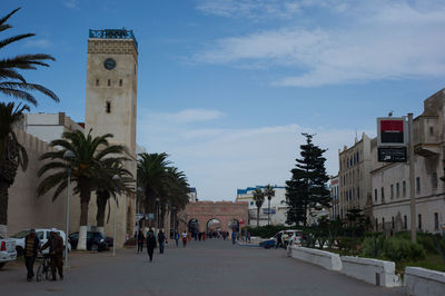 People on street amidst buildings in city against sky