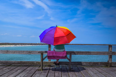 Rear view of woman with colorful umbrella looking at sea against sky
