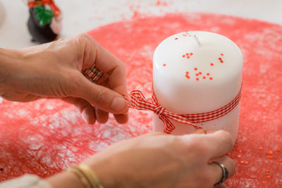 Cropped image of woman tying ribbon on candle during christmas