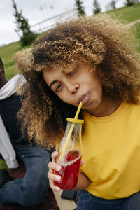 Young woman drinking lemonade by friend in park