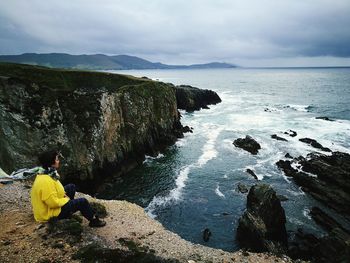 People sitting on rock by sea against sky