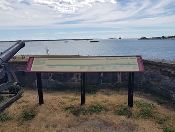 Bench on field by sea against sky