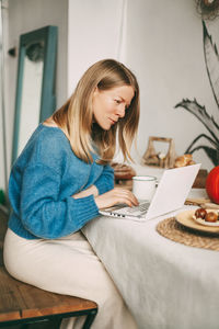 Cute blonde girl working in the morning on a laptop and drinking coffee. work online, freelance