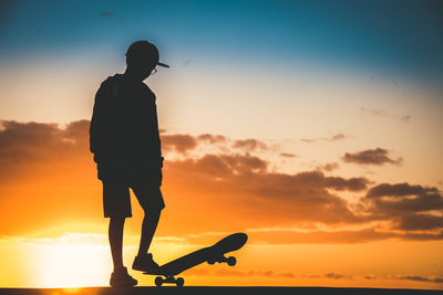 Silhouette boy with skateboard against sky during sunset