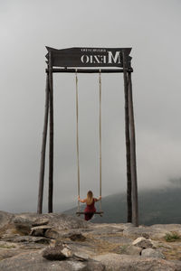 Rear view of woman sitting on rope swing against sky