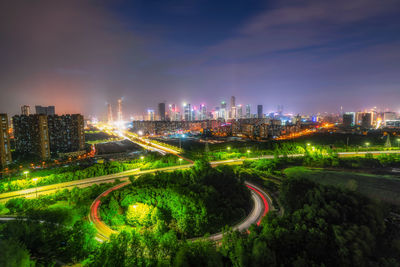 Illuminated road amidst buildings against sky at night