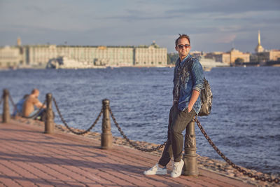 Portrait of boy standing on riverbank against sky in city