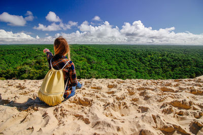 Rear view of woman sitting on sand against forest