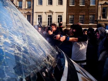 Protestors breaking windshield of vehicle against building