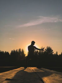 Silhouette man standing on road against sky during sunset