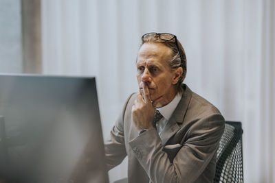 Mature businessman with hand on chin looking at computer monitor in office