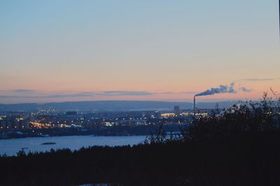 Illuminated cityscape by sea against sky at sunset