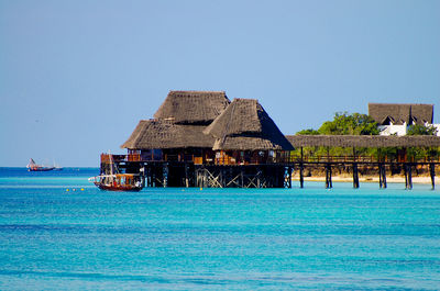 Stilt house by sea against clear blue sky