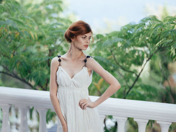 Young woman looking away while standing against railing