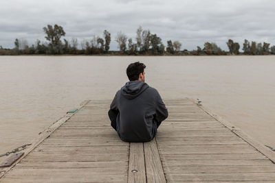 Rear view of man sitting on wooden pier