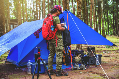 Side view of man with backpack standing by tent in forest