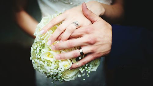 Cropped hands of bride and groom holding white rose bouquet