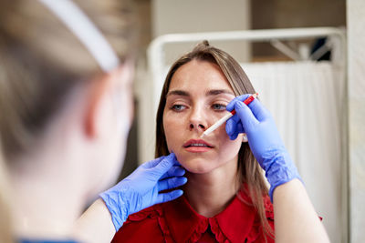 Blur beautician in latex gloves drawing line with white pencil while correcting shape of lips of young woman during work in aesthetic clinic