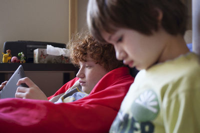 Boy using tablet computer while sitting by brother at home