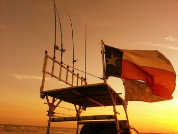 Low angle view of texas state flag with fishing rods on platform against sunset sky