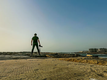 Rear view of man standing on beach against clear sky